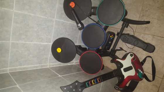 Black Xbox 360 with drums with drumsticks and peddle, guitar with guitar strap and pick, microphone,